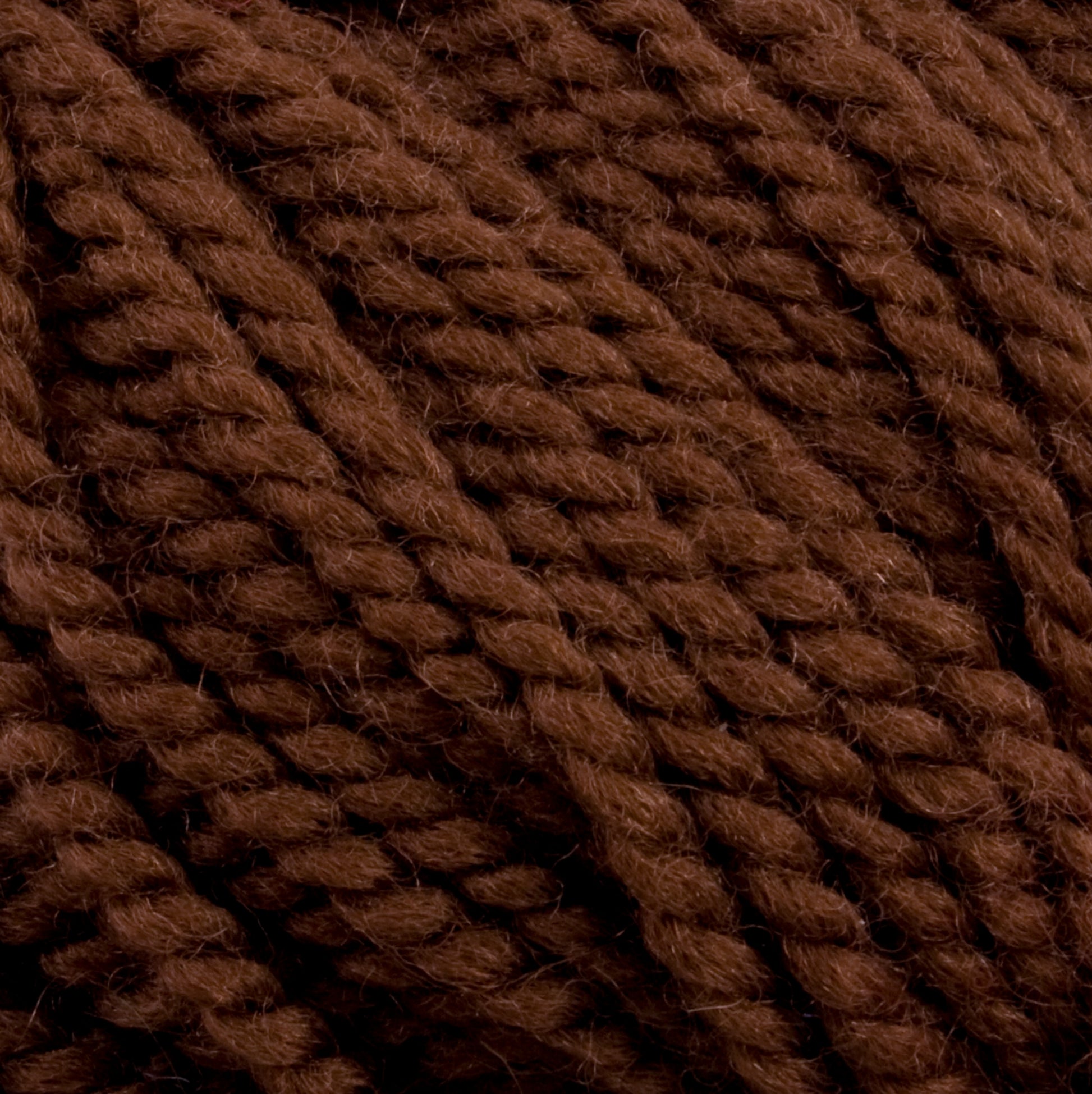 Close-up image of Norumbega yarn fibers wound together. The texture appears soft and slightly fuzzy, with individual strands clearly visible in a tightly twisted formation. Made from 100% U.S. wool, the color is a rich, deep brown and exudes the quality of Caledonian Dye Works' Aran weight yarn.