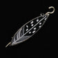 The Songbird Shawl Pin by Bonnie Bishoff Designs is a black and white enamel brooch shaped like a leaf, featuring intricate feather-like patterns and oval dots. This handmade gift is beautifully outlined in silver and includes a locking pin for secure fastening. The background of the brooch is solid black, making it an elegant piece from the Bonnie Bishoff collection.