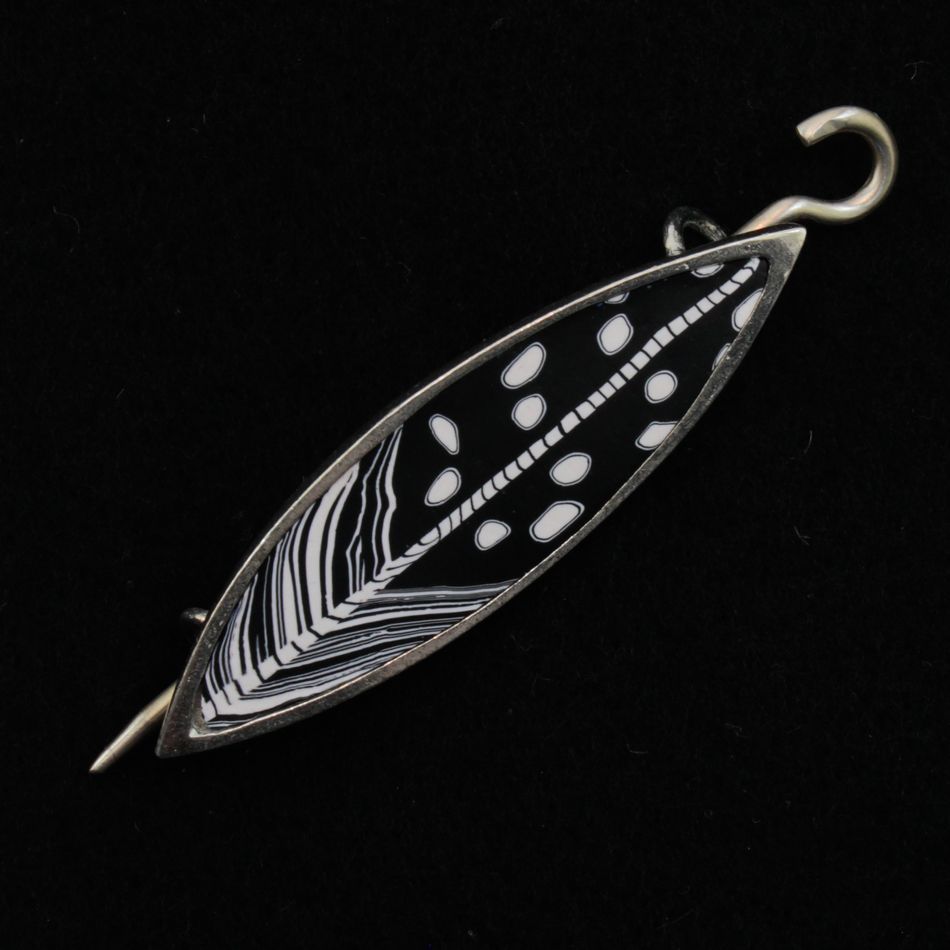 The Songbird Shawl Pin by Bonnie Bishoff Designs is a black and white enamel brooch shaped like a leaf, featuring intricate feather-like patterns and oval dots. This handmade gift is beautifully outlined in silver and includes a locking pin for secure fastening. The background of the brooch is solid black, making it an elegant piece from the Bonnie Bishoff collection.