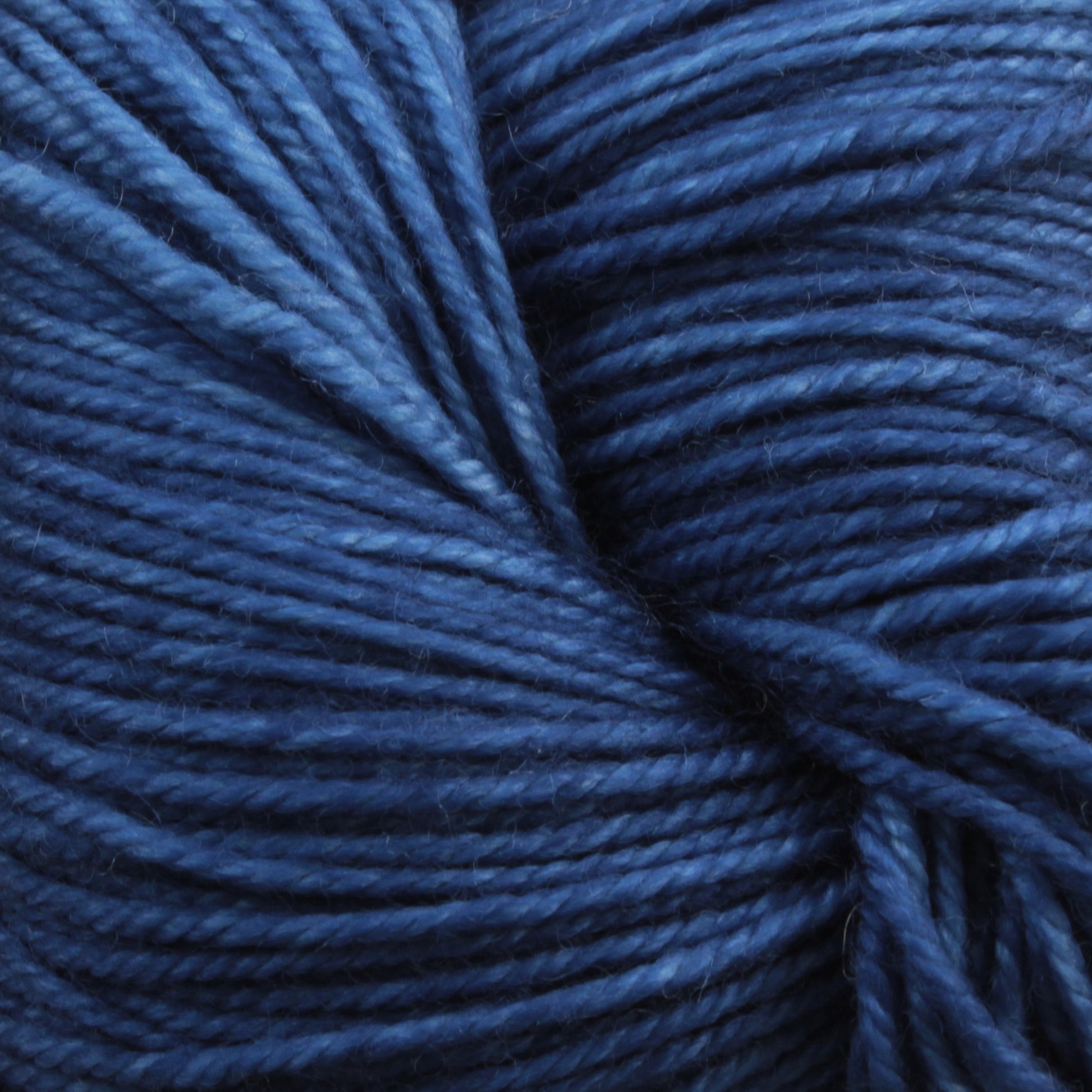 Close-up image of tightly wound Malabrigo Sock yarn by Malabrigo Yarn, showcasing various shades of dark and light blue Merino wool, creating a textured and detailed view of the fibers.