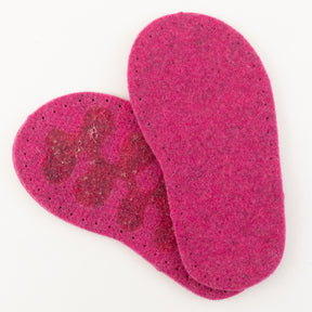 Two pink Children's Thick Felt Slipper Soles w/Latex Grip by Joe's Toes are displayed overlapping on a white background. The top sole features patches of a darker shade and visible perforations around the edges. The texture of the bottom sole is showcased in detail, emphasizing their eco-friendly design.