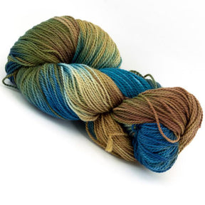 The Great Adirondack Organic DK Cotton from Great Adirondack Yarn Co, Inc. features a skein of hand-dyed, multicolored yarn, showcasing a blend of earthy greens and browns with vibrant blues. This organic cotton yarn is coiled and twisted, resulting in a visually appealing array of variegated colors and textures on a white background.