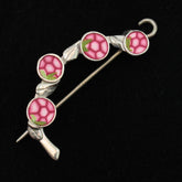 Introducing the Spring Bud Shawl Pin by Bonnie Bishoff Designs, a decorative brooch from Bonnie Bishoff. This elegant piece features a silver frame housing four circular pink tiles resembling flowers, each adorned with a hexagonal pattern and small green leaves, set against a black background. Crafted with polymer clay design for intricate detail, the shawl pin boasts a curved style and an attached locking pin for secure fastening.