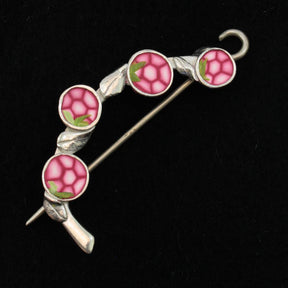 Introducing the Spring Bud Shawl Pin by Bonnie Bishoff Designs, a decorative brooch from Bonnie Bishoff. This elegant piece features a silver frame housing four circular pink tiles resembling flowers, each adorned with a hexagonal pattern and small green leaves, set against a black background. Crafted with polymer clay design for intricate detail, the shawl pin boasts a curved style and an attached locking pin for secure fastening.