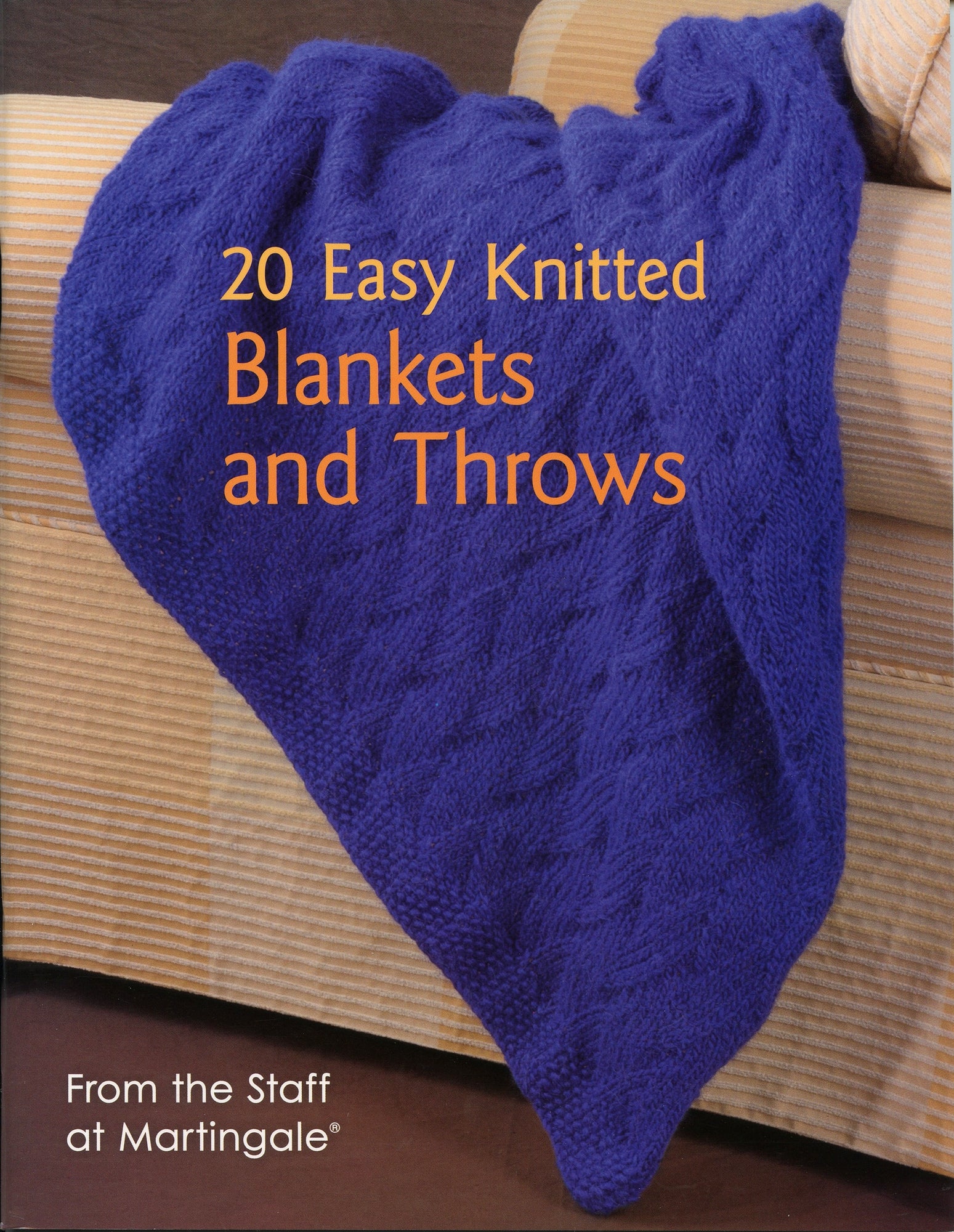 The cover of the knitting book titled "20 Easy Knitted Blankets and Throws" from Martingale & Co showcases a vibrant purple knitted blanket elegantly draped over a beige sofa. The subtitle reads "From the Staff at Martingale," offering delightful throw patterns and knitted blanket patterns for all skill levels.