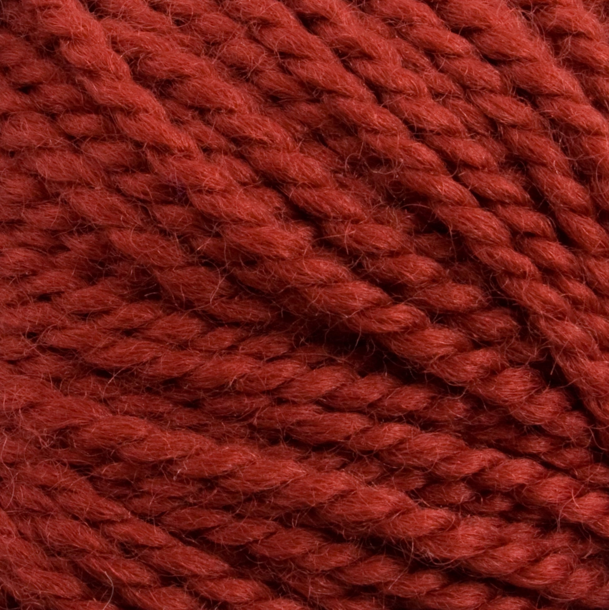 Close-up image of thick, red Aran weight yarn strands tightly wound together. The texture is soft and slightly fuzzy, showing detailed fiber twists. The yarn appears to be 100% U.S. wool or a similar material, often used for knitting or crocheting projects; it’s the Norumbega yarn by Caledonian Dye Works.