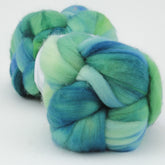 Two bundles of Nube by Malabrigo yarn, under the renowned Malabrigo Yarn brand, showcasing a mesmerizing blend of green, blue, and white shades. The fibers are tightly packed and twisted, creating a soft and fluffy texture. Set against a white background, the vibrant colors of the merino wool truly stand out.