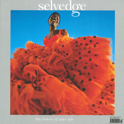 A person is smiling while wearing a voluminous, orange ruffled dress with black spots. The cover of *Selvedge - Issue 107: High Summer* features the word "selvedge" prominently at the top, with the tagline "The Fabric of Your Life" at the bottom against a blue sky background, setting a vibrant tone for any fashion agenda.