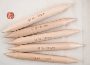 Four of Accessories Unlimited's Double-Point Bamboo Knitting Needles, Jumbo, labeled "US 36 - 20.00mm," are arranged in a row on a cream-colored fabric. A penny is placed beside the lightweight needles for size comparison, making them perfect for working with chunky yarns.