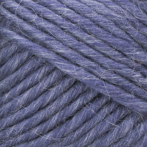 Close-up of Lamb's Pride Bulky Yarn by Brown Sheep reveals thick, soft, blue threads with a slightly fuzzy texture. The tightly wound strands display shades of lighter and darker blue, likely due to natural light and shadow. Ideal for knitters and crocheters, the fibers are clearly visible, highlighting the yarn’s fluffiness and softness.