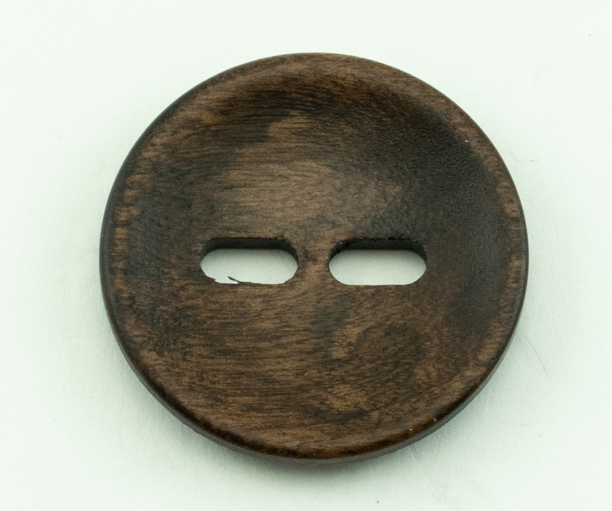 A close-up image of the "Wood Foxeye" round wooden button by Buttons Etc., featuring a 1 3/8" diameter and two horizontal holes in the center, lying flat on a white background. The wood grain and natural coloration give a textured and rustic appearance to the button.