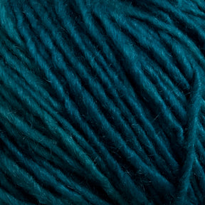 Close-up image of Malabrigo Silky Merino in deep teal from Malabrigo Yarn. The yarn features a textured surface with threads tightly wound together, showcasing its fiber details and color variations from lighter to darker teal shades. This exquisite blend includes hints of silk, adding an extra touch of elegance.