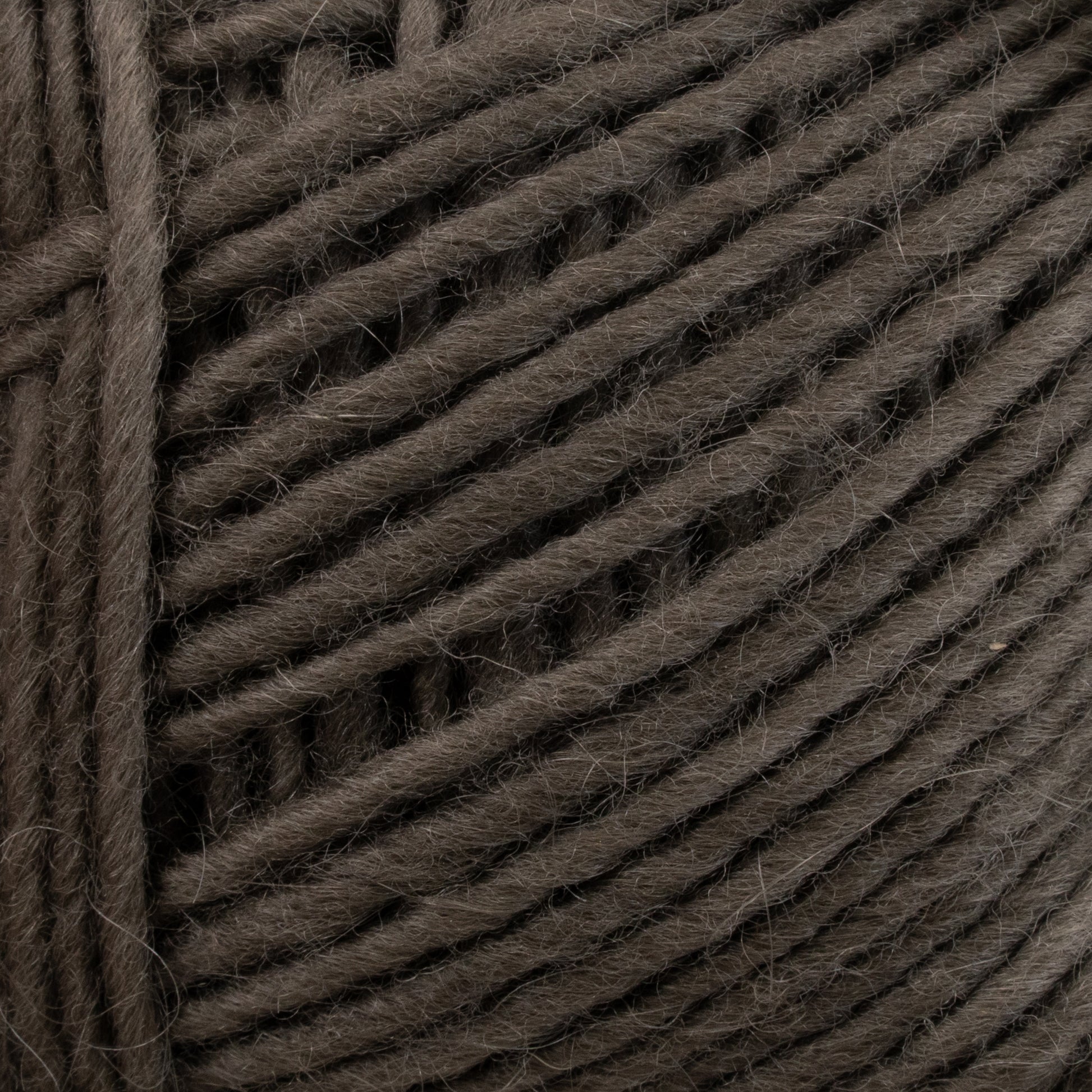 Close-up of a ball of dark gray Brown Sheep Lamb's Pride Worsted Yarn. The texture is clearly visible, showcasing its thickness and the interwoven strands. Ideal for felting projects, the yarn appears soft and slightly fuzzy.