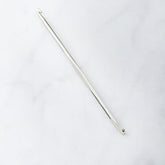 A single Cocoknits Stitch Fixer, featuring a metal crochet hook with a small hook on one end and a slight groove near the other, ideal for knitting project repairs, placed on a light, smooth surface.