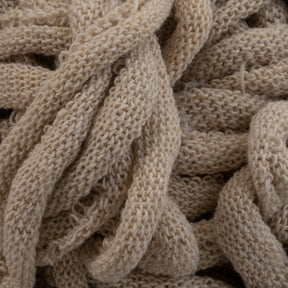 Close-up view of intertwined, chunky beige yarn on the Harrisville Potholder Loops - Traditional Size Mini Pack from Friendly Loom. The texture is soft and slightly fuzzy, showcasing a tight, intricate knit pattern. Neatly bundled in a random, looping arrangement, the yarn highlights the craftsmanship achievable with traditional looms.