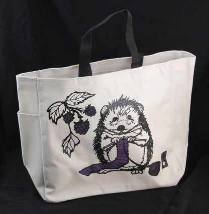 The Hedgehog Project Tote by Mum n Sun Ink from Bonnie Bishoff is a white Envirotote canvas bag with black straps, adorned with a charming illustration of a hedgehog knitting a purple scarf. The hedgehog is surrounded by a branch of blackberries, creating an enchanting scene against the solid black background. Designed in New Hampshire, this tote bag combines functionality with whimsical charm.