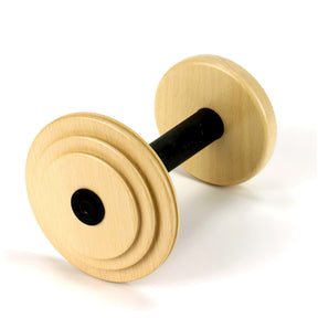 The Louët Bulky Bobbin by Louët Inc. is a wooden cylindrical object with a black handle in the center, resembling a dumbbell. The ends are circular and smooth, featuring concentric circles carved into the surface that give it a distinct, grooved design. The bobbin rests on a white surface.