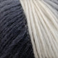 Close-up image of thick, multi-colored self-striping yarn transitioning from dark gray on the left to off-white on the right, showing the texture and interwoven strands. The fibers appear soft and fluffy, suggesting a cozy wool and silk blend ideal for knitting or crocheting. This is Louisa Harding Amitola Grande by Knitting Fever / Euro Yarns.