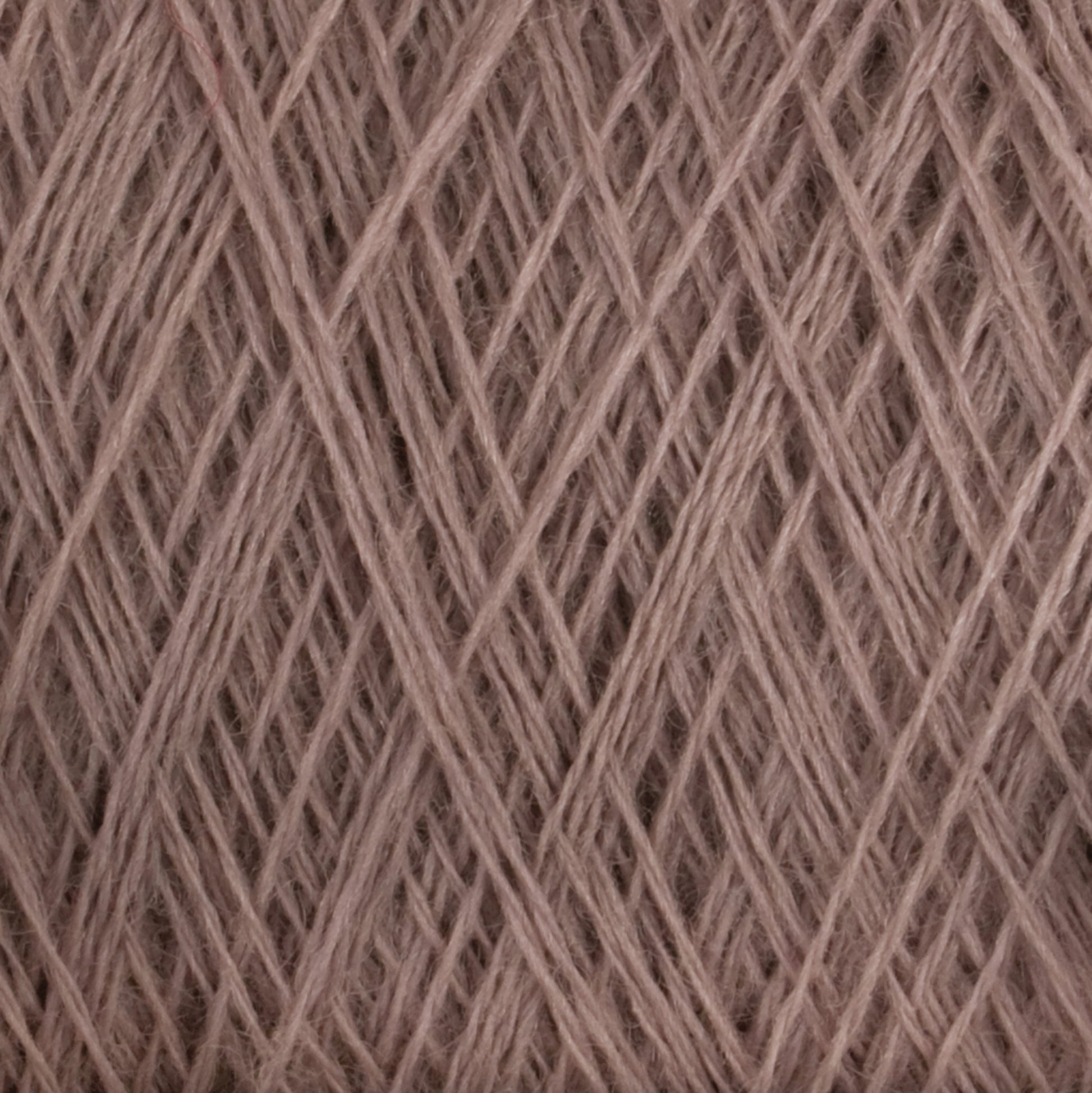 Close-up of JaggerSpun Maine Line 2/20 Yarn in beige. The tightly wound fibers from Jagger Brothers, Inc. create a textured pattern with intersecting lines and overlapping strands, giving a crisscross effect. The yarn appears soft and slightly fuzzy.