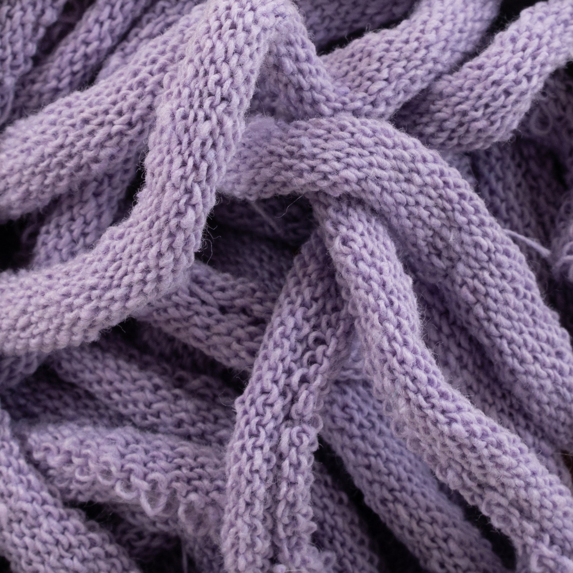 Close-up view of intertwined lengths of soft, lavender-colored Harrisville Potholder Loops from Friendly Loom. The texture is plush and looped, resembling the intricate knit patterns typically crafted on a standard loom, showcasing the gentle, cozy nature of this Traditional Size Mini Pack material.