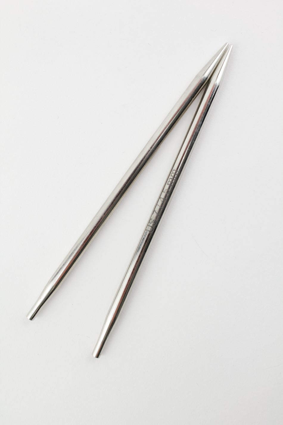 Two Nova Platina Interchangeable Knitting Needles, 4.5" Tip by Accessories Unlimited, are crossed against a white background. The stainless steel needles have pointed tips and boast a smooth and shiny finish.