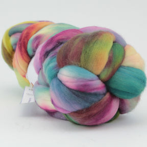 Introducing Nube by Malabrigo from Malabrigo Yarn: a lush braid of multicolored, hand-dyed merino wool roving featuring vibrant hues of green, purple, pink, yellow, and blue. The fibers are soft, fluffy, and perfectly suited for spinning or felting projects. Neatly coiled against a plain white background, this roving is a must-have for your next creative endeavor.