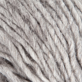 Close-up image of Jöklalopi (Bulky Lopi) yarn in grey by Berroco, Inc. showcases its soft, slightly fuzzy texture. The loosely twisted strands reveal individual fibers and their natural imperfections, exuding a rustic handmade charm. The neutral color and unique texture suggest it is ideal for knitting or crocheting cozy garments like chunky winter sweaters.