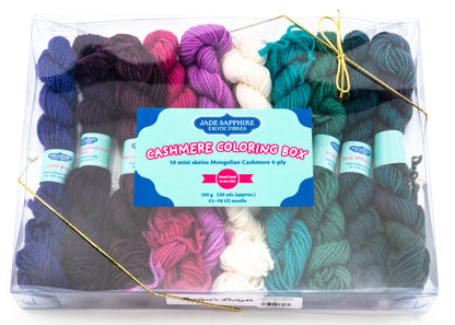 A clear plastic box containing 10 mini skeins of Mongolian cashmere in an array of colors, including shades of purple, pink, teal, green, and black. The label reads "Cashmere Coloring Box Yarn Pack" by Jade Sapphire Exotic Fibres, making it the ideal knitting kit for any project.