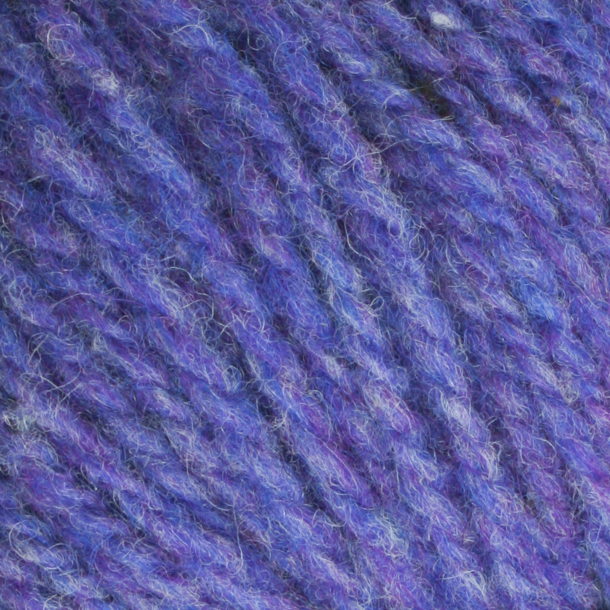 Close-up image of a textured blue and purple worsted weight yarn, showing interwoven fibers and a soft, fuzzy surface. The mix of heathered colors creates a mottled effect, highlighting the intricate strands and the overall fluffy appearance of Bartlettyarns Maine Wool Yarn from Bartlettyarns.