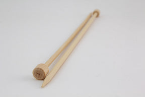 A pair of 12" Bamboo Single-Point Knitting Needles from Accessories Unlimited are placed parallel on a white surface. One needle has a rounded end with a flat, circular top, while the other end is pointed for knitting. These single-point needles are light in color and have a smooth finish.