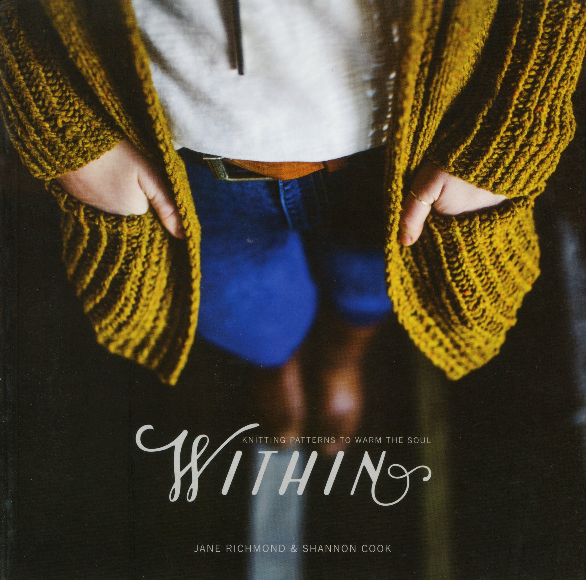 A person wearing a mustard yellow knitted cardigan stands with their hands in their pockets. They are paired with blue jeans and a white shirt. The cover text reads, "Within: Knitting Patterns to Warm the Soul" by Jane Richmond and Shannon Cook under the Never Not Knitting brand, featuring everyday garments and accessories.