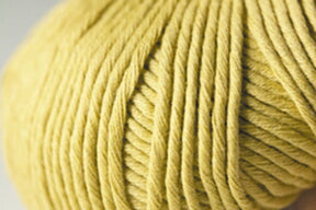 Close-up of a ball of yarn in a soft yellow color. This Jo Sharp Desert Garden Aran Cotton by Kingfisher Yarn & Fibre is neatly wound, creating a textured pattern. The background is out of focus, emphasizing the details and its suitability for knitting performance.