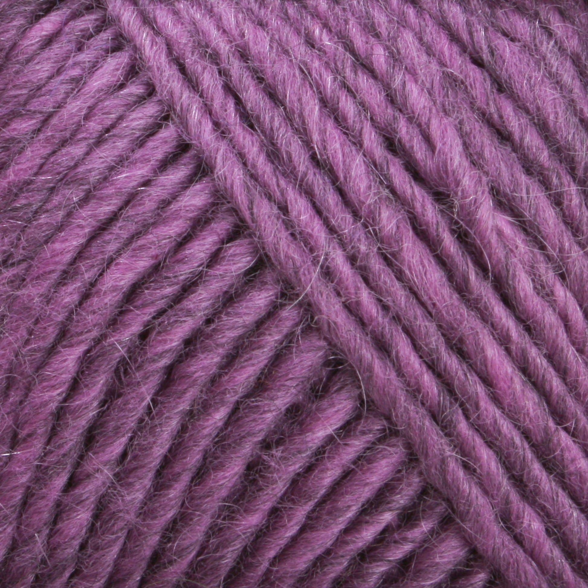 Close-up image of textured purple yarn, tightly wound in a skein. The strands appear soft and thick, showcasing a rich, vibrant hue with subtle variations in color. Ideal for felting projects with Lamb's Pride Worsted Yarn by Brown Sheep, the image highlights the detailed fibers and the plush, cozy appearance of the yarn.