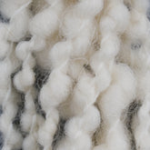 A close-up view of Polar Bear Yarn by Henry's Attic reveals thick, white, fluffy weaving yarn with twisted and looped strands that create a textured and soft appearance. The dense and intertwined fibers highlight its cozy and cushioned quality—perfect for adding an accent in the warp or using with a 4-6 dent reed.