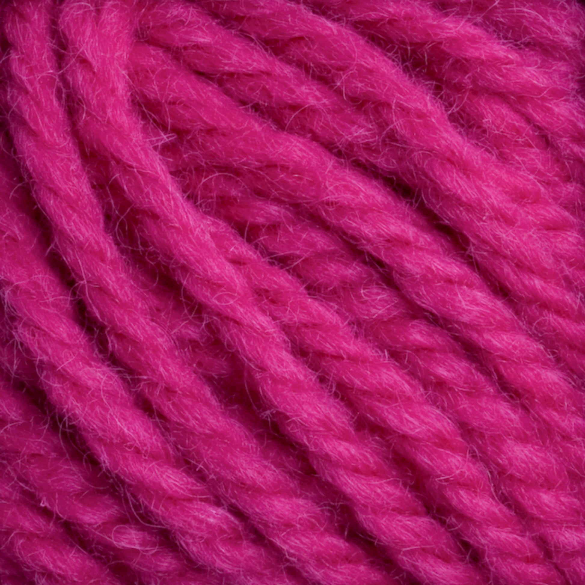 Close-up of multiple strands of bright magenta Halcyon Yarn Classic Rug Wool by Caledonian Dye Works, showcasing the texture and fiber detail. The yarn is thick and appears soft, with some visible fuzziness. Ideal for rug weavers, the hand-dye process enhances its vivid color. The strands are loosely coiled together.