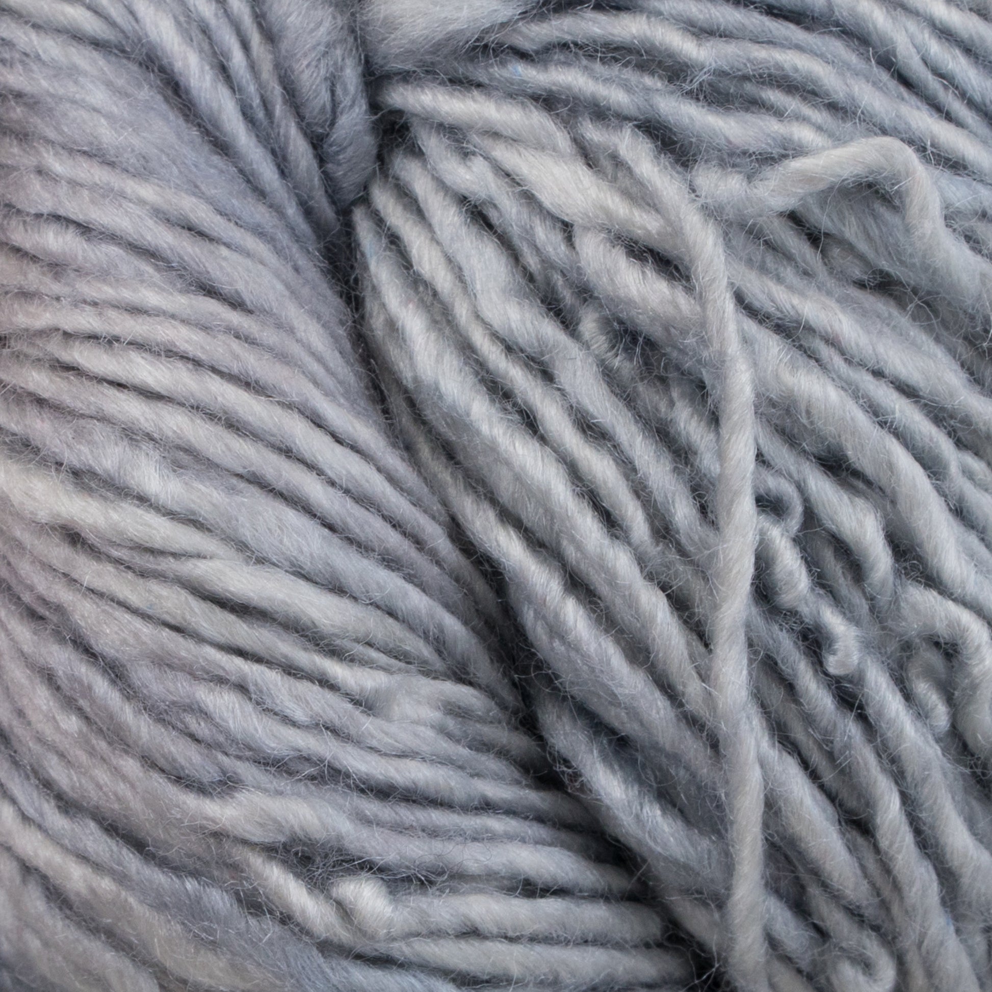 Close-up of a skein of Malabrigo Silky Merino by Malabrigo Yarn. The soft, thick, light grey yarn is coiled with visible texture, showcasing its slightly fluffy and smooth fibers.