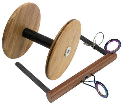 The Majacraft Wild Flyer with Bobbin by Majacraft Co. is a tool often utilized in fly tying. It boasts a large wooden bobbin mounted on a dark cylindrical shaft, which is connected to a rectangular wooden base. The setup also includes vibrant scissor-like tools clipped onto the base for added convenience.