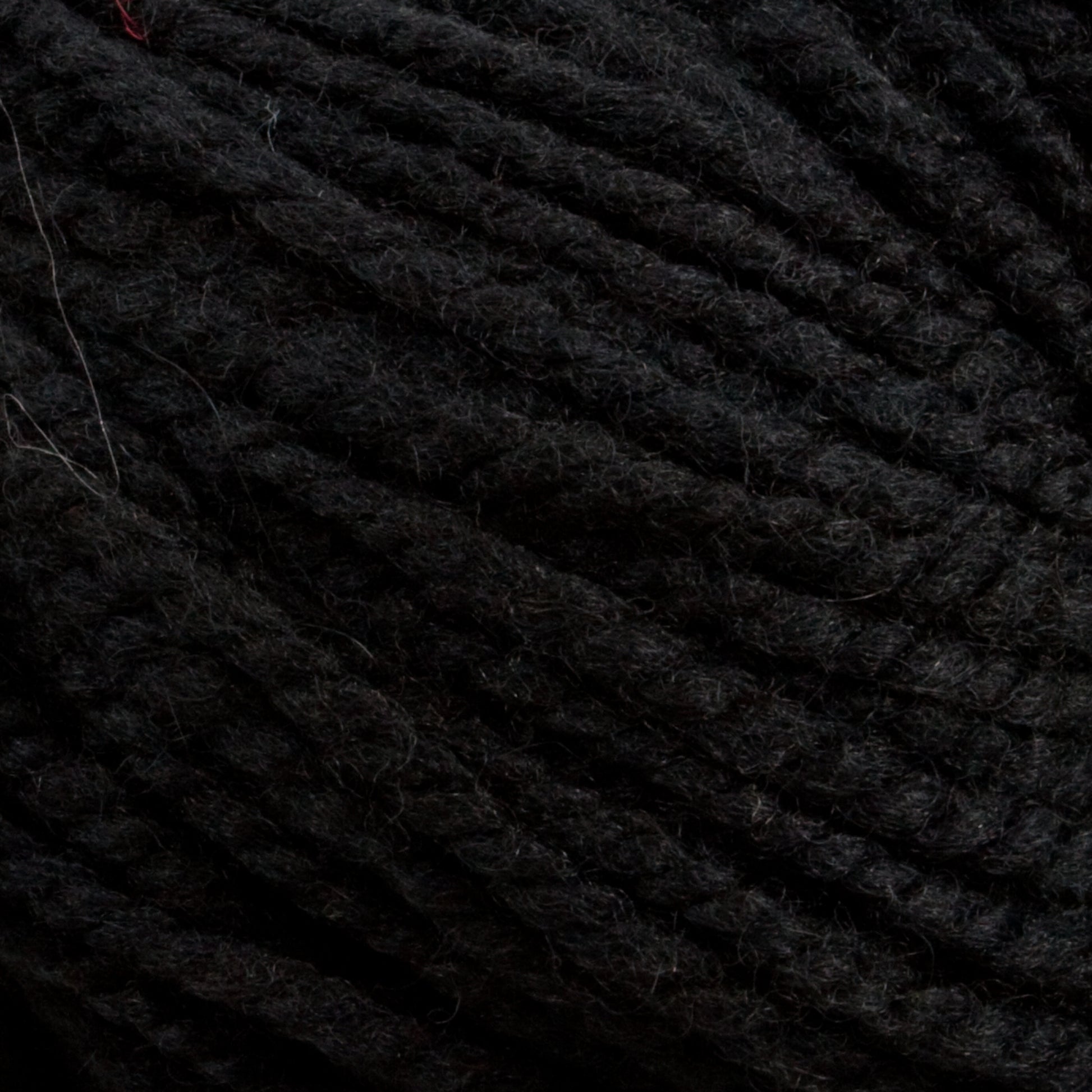 Close-up of a ball of black, Tuffy Canadian Sock Yarn by Briggs & Little with tightly wound fibers. The texture is clearly visible, showing fine threads and slight fuzziness common to woolen materials. A single strand of white fiber is caught in the yarn.