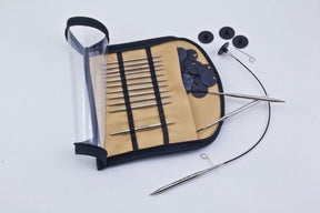 An Accessories Unlimited Nova Platina Interchangeable Circular Knitting Needle Set is displayed on a white background. The set includes a range of metal interchangeable knitting needles made from hollow brass pipes in various sizes, cables, and stoppers, all neatly organized in a zippered case with a transparent cover.