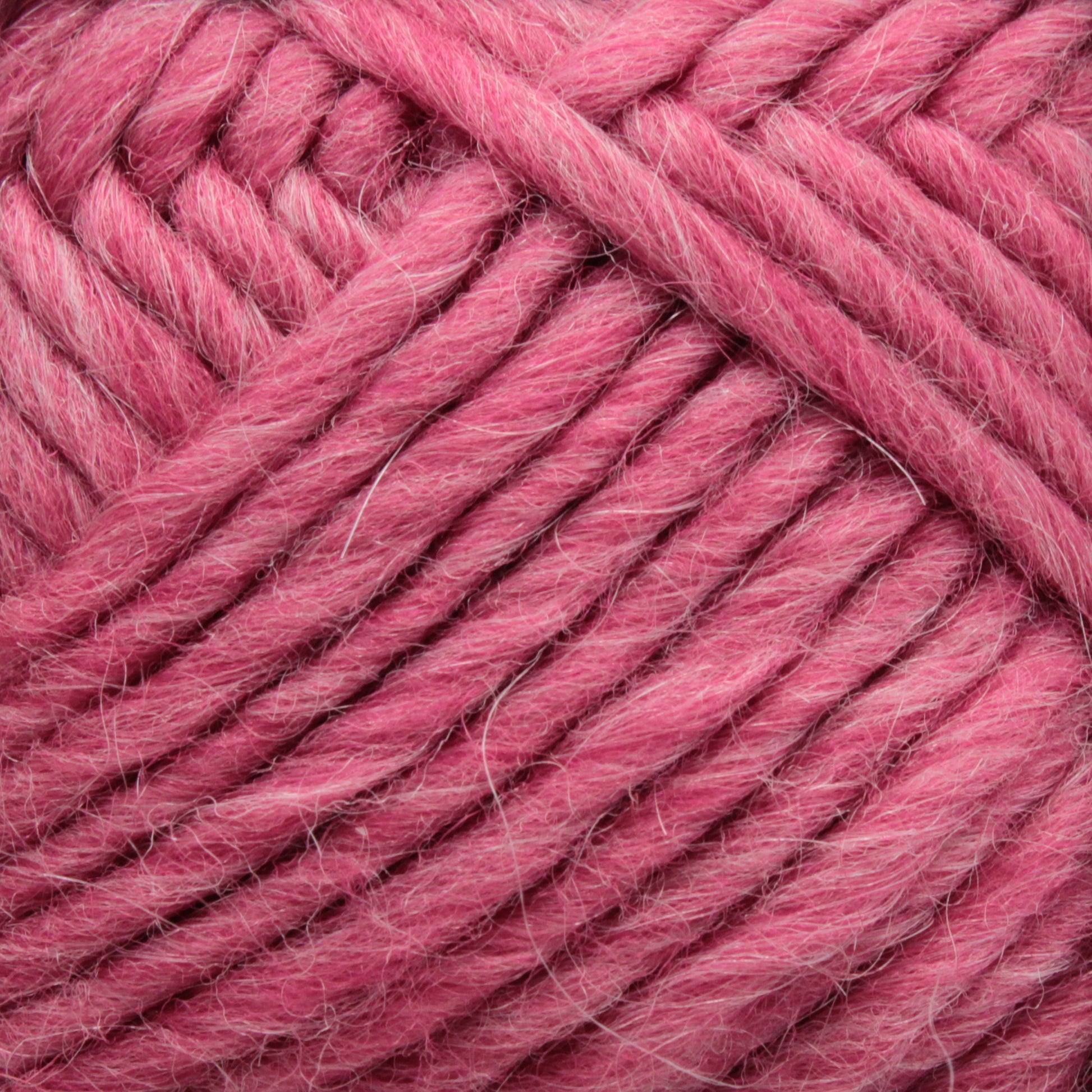 Close-up of a ball of Lamb's Pride Bulky Yarn in a vibrant pink hue, showing intricate details of the woven fibers and texture. The yarn, by Brown Sheep, appears soft and thick, ideal for knitters and crocheters crafting cozy woven blankets. The image emphasizes the cozy and vibrant shade of this high-quality yarn.