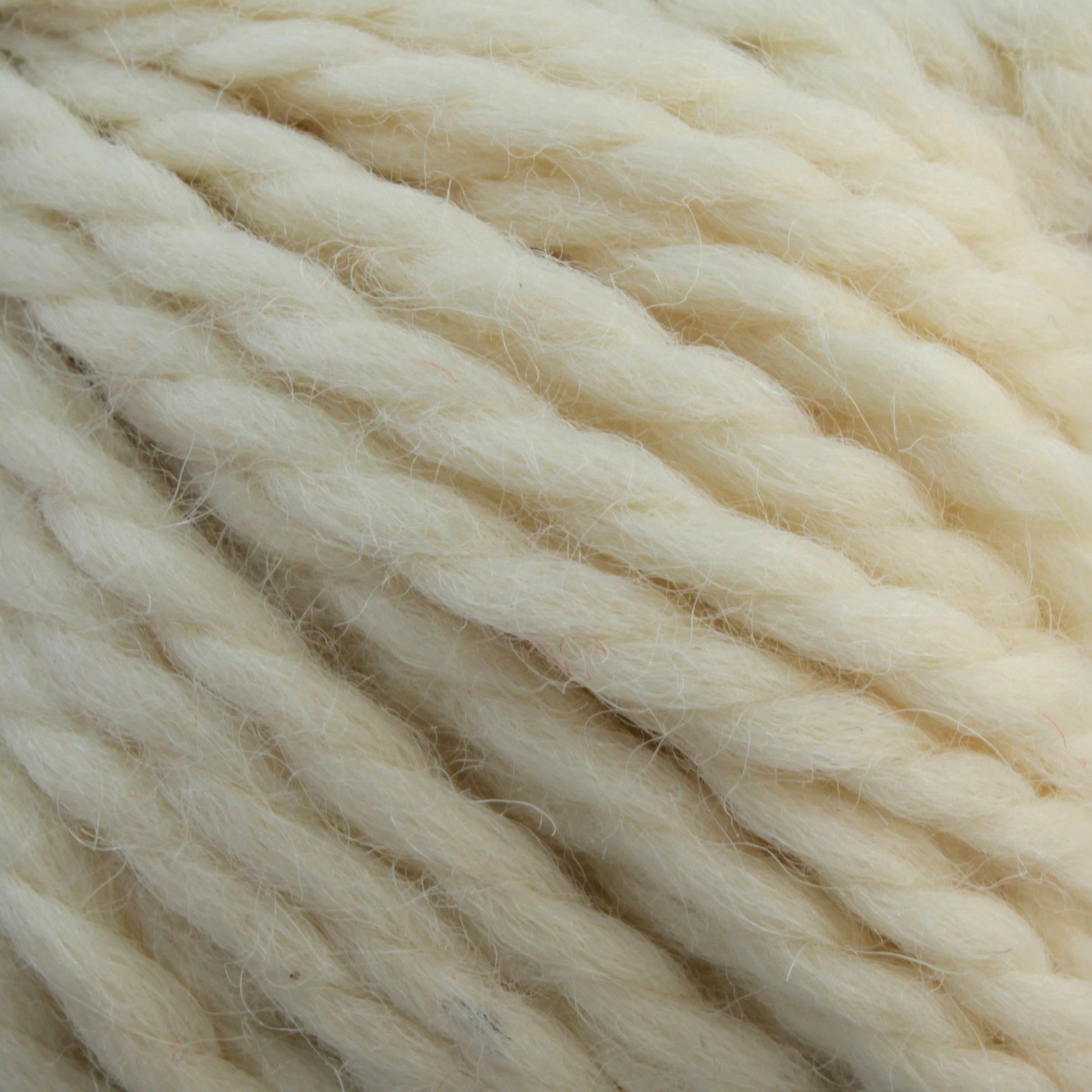 Close-up of thick, cream-colored Baby Alpaca Grande yarn twisted together, showing the texture and strands in detail. The ultra-soft yarn from Plymouth Yarn Co. appears perfect for knitting or crocheting cozy garments and accessories. The color is uniform and light, with slight variations in shade, ideal for bulky weight projects.