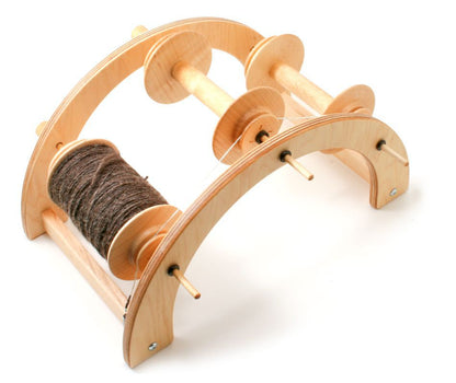 The Schacht "Industrious" Tensioned Lazy Kate by Schacht Spindle Co. is a wooden yarn winder that comes with two empty bobbins and one partially wound with dark brown yarn. Designed with an arch-shaped frame, it effortlessly holds multiple spools for winding or unwinding, making it an ideal spinning accessory.