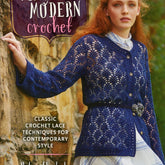 A woman with long, wavy red hair leans against a stone wall, adorned in a dark blue lace crochet cardigan over a white dress with blue stripes. The book titled "Vintage Modern Crochet" by Ingram Content highlights classic crochet lace techniques.