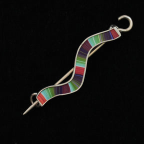 The Stripe Wavy Shawl Pin by Bonnie Bishoff Designs is a beautiful silver S-shaped pin featuring colorful, horizontal stripes in shades of green, red, purple, and blue. It has a glossy finish and is set against a black background. This handmade piece by local artisan Bonnie Bishoff captures the charm of meticulously crafted knitted wearables.