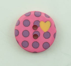 The Dots Button by Buttons Etc. is a round, pink 5/8" plastic button adorned with purple polka dots and featuring two central holes. Adding a decorative touch, it also has a small yellow heart on the right side. The button is displayed against a pale, light-colored surface.