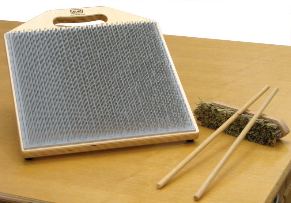 The Louët Blending Board 12"x12" (30cmx30cm) by Louët Inc., a unique musical instrument with vertical metal tines set in a square wooden frame, is displayed on a wooden surface. Accompanying it are two wooden sticks and a soft bristle brush—tools designed for playing the instrument. This innovative blending board offers a delightful range of sounds.