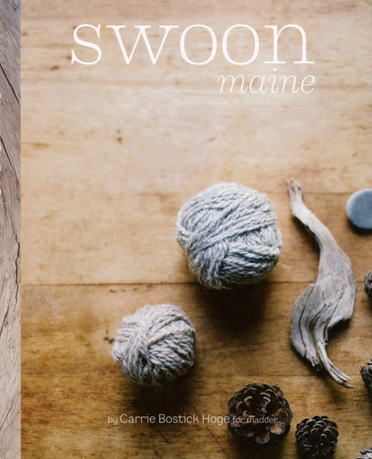 The cover of the Never Not Knitting book "Swoon Maine" by Carrie Bostick Hoge beautifully showcases two balls of gray yarn, a pinecone, and a piece of driftwood artfully arranged on a wooden surface. The title is written in white text at the top, perfectly capturing the essence of knitwear photography.