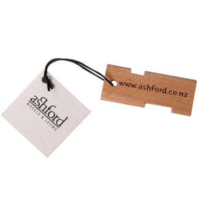 An Ashford Yarn Gauge, made of wood with the URL "www.ashford.co.nz" engraved on it, is attached to a white tag by a black cord. The tag, displaying the text "Ashford Wheels & Looms" in a stylized font, makes for a perfect fiber artist tool.