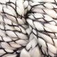 Close-up image of Malabrigo Caracol, a chunky white super bulky yarn from Malabrigo Yarn. Thin black threads are intertwined, creating a textured and cozy appearance. The fibers appear soft and plush, made from superwash merino wool. Perfect for knitting or crocheting warm garments or accessories.