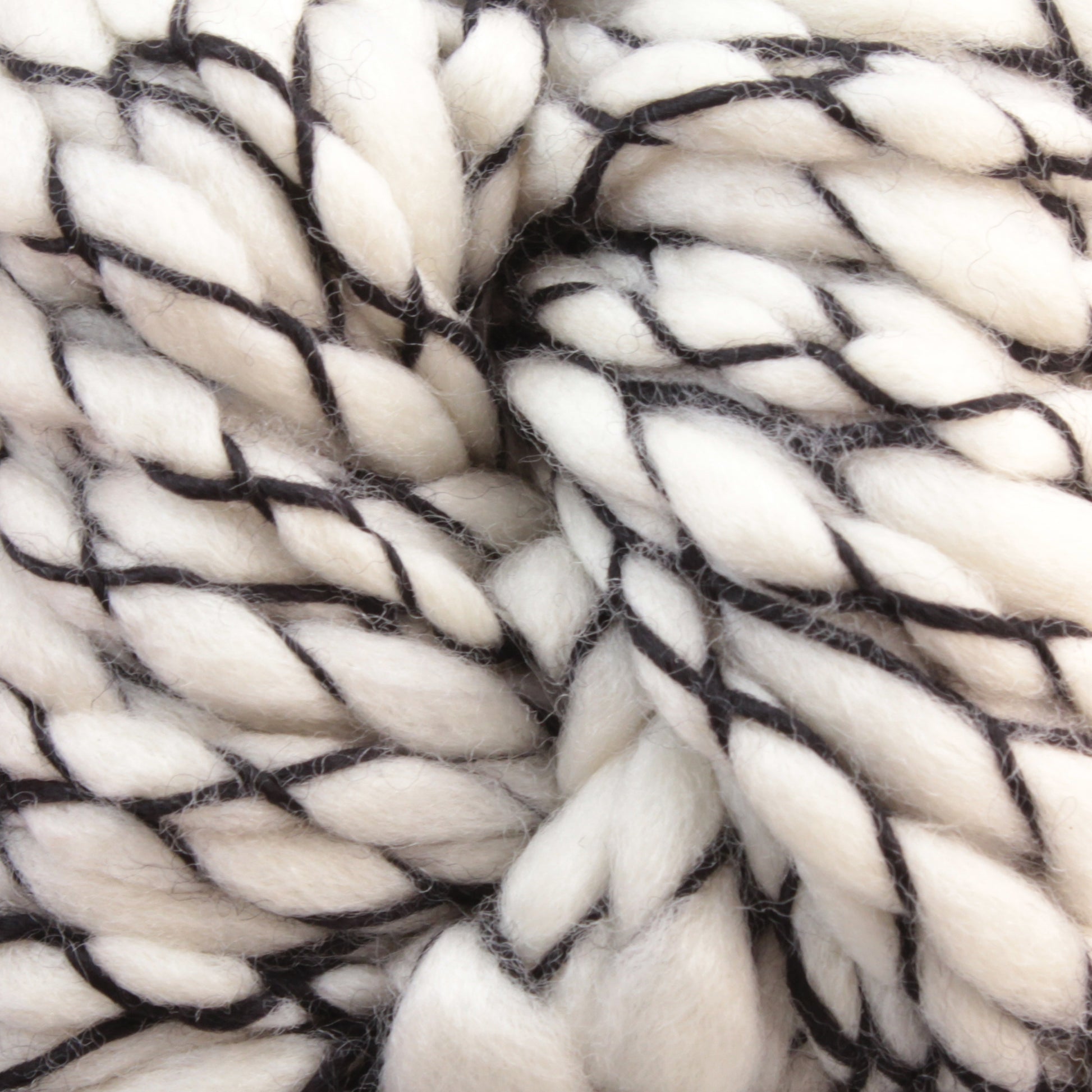 Close-up image of Malabrigo Caracol, a chunky white super bulky yarn from Malabrigo Yarn. Thin black threads are intertwined, creating a textured and cozy appearance. The fibers appear soft and plush, made from superwash merino wool. Perfect for knitting or crocheting warm garments or accessories.